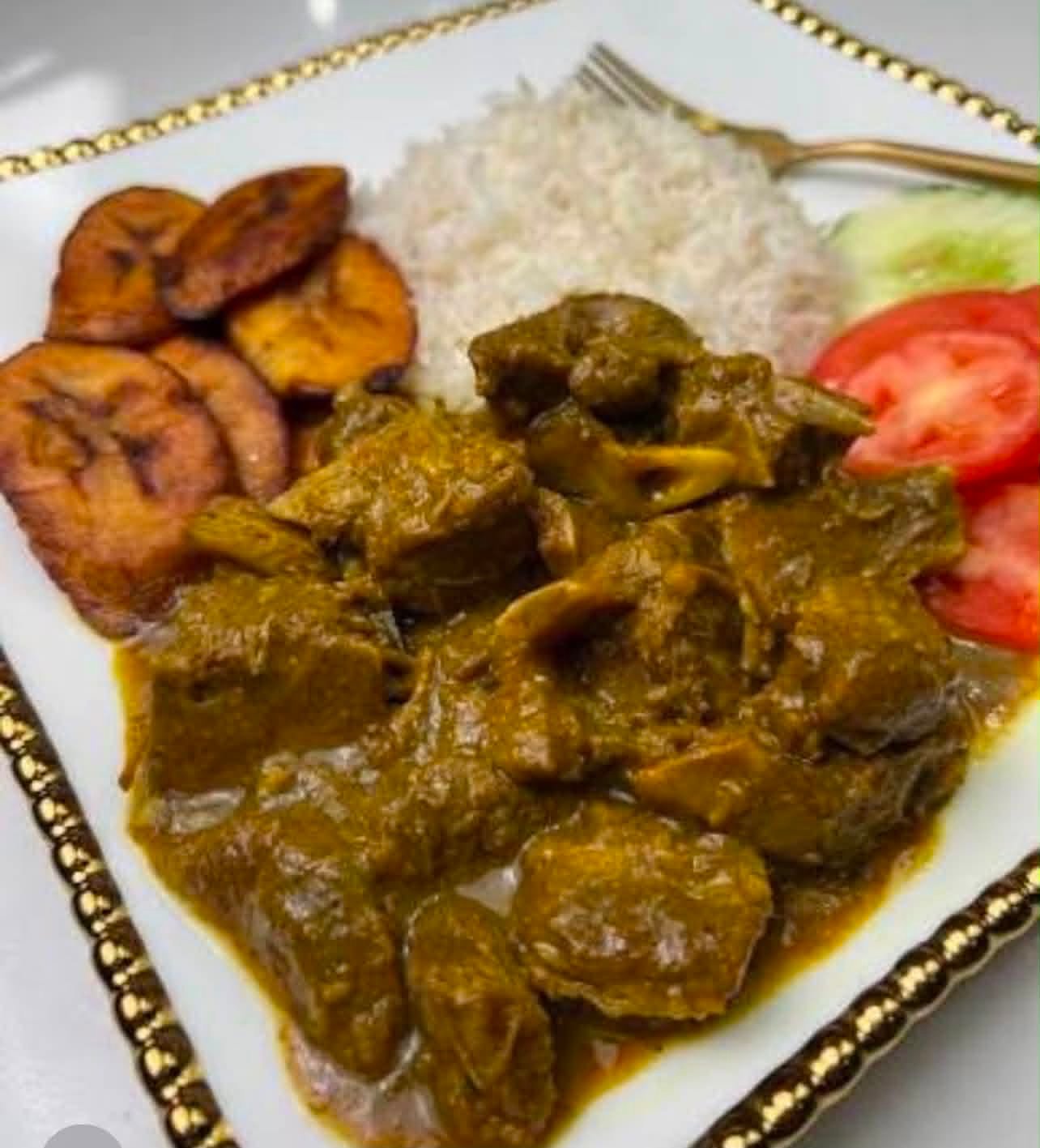 Rena's curry goat served with white rice, fried plantains, tomato and cucumber